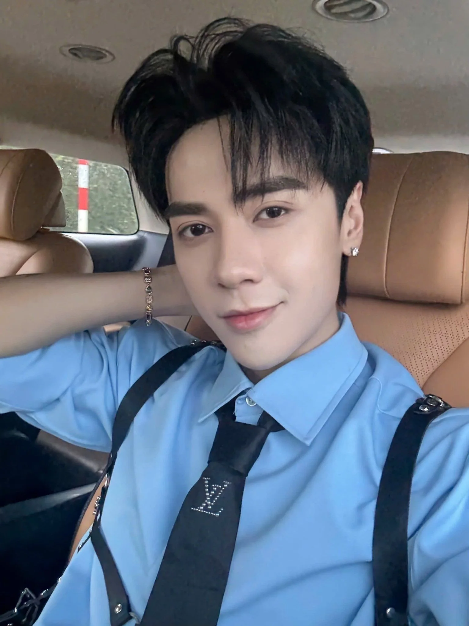 Ảnh Quang Hùng ngồi trong xe hơi, diện bộ đồ vest với dây nịt da màu đen, biểu cảm nam tính và cuốn hút